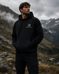 A man wearing a black pullover hoodie with a white circular 'MORPHATRAIL' logo on the chest, standing in a mountainous outdoor setting.